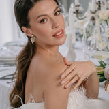 A bride wearing elegant white attire with long sleeves, featuring the Lettie Bridal Stud Swarovski Crysal Earrings with cascading crystals.