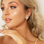 A woman wearing a pair of leaf-shaped crystal earrings with 18K gold or rhodium plating.