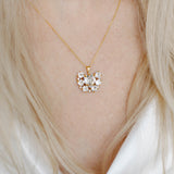 A person wearing a white v-neck top showcasing a gold-plated necklace with a floral pattern and a central heart-shaped crystal pendant.