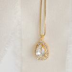 A gold-plated necklace with a teardrop-shaped pendant detailed with crystals, displayed by Sarah Gauci