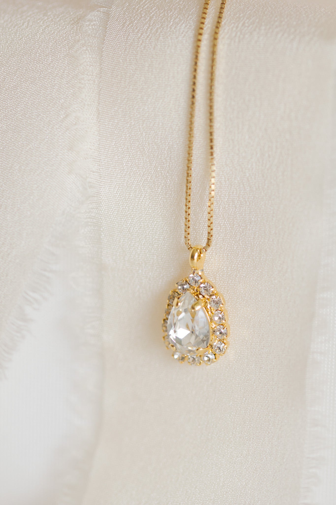 A gold-plated necklace with a teardrop-shaped pendant detailed with crystals, displayed by Sarah Gauci