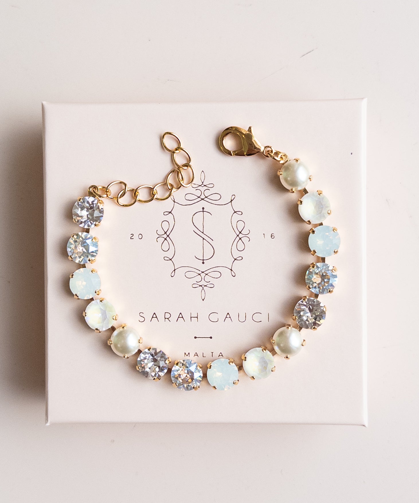 Bracelet with opal stones on a pink box with 'Sarah Gauci' branding