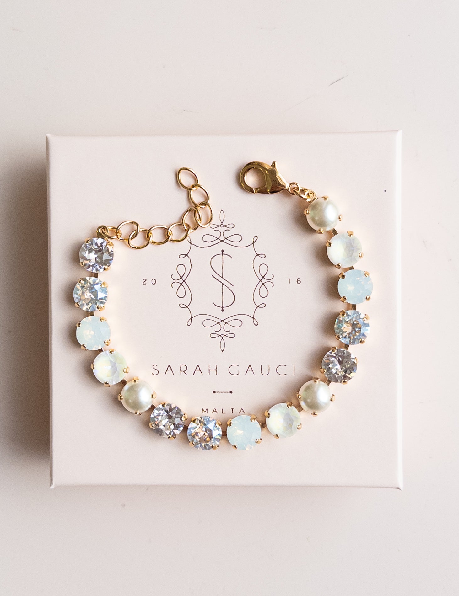 Bracelet with opal stones on a pink box with 'Sarah Gauci' branding