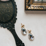 Vintage-style hand mirror, pink flower, and crystal earrings on a light surface.