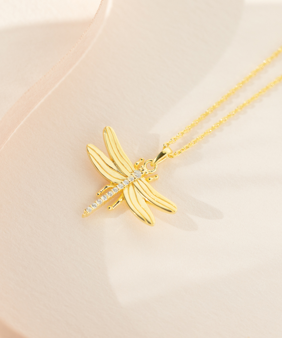 A gold-plated sterling silver necklace with a cubic zirconia pendant shaped like a dragonfly, displayed on a pale background.