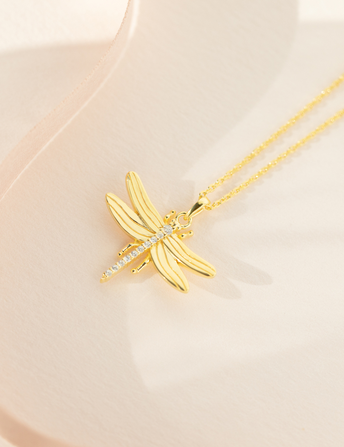 A gold-plated sterling silver necklace with a cubic zirconia pendant shaped like a dragonfly, displayed on a pale background.
