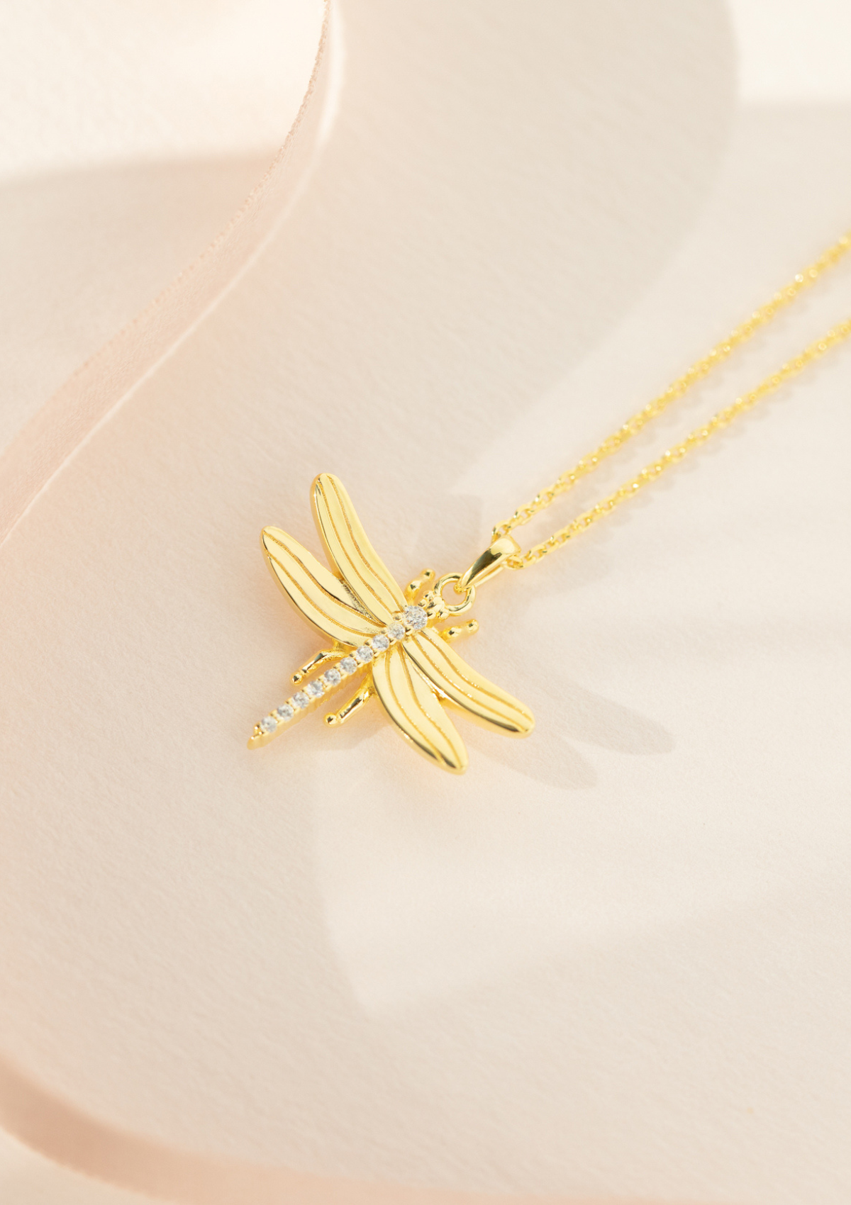 A gold-plated sterling silver necklace with a cubic zirconia pendant shaped like a dragonfly, displayed on a pale background.