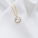 A gold-plated necklace with a round pendant, handset with beautiful crystals, displayed on a white fabric surface.