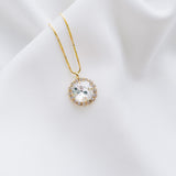A gold-plated necklace with a round pendant, handset with beautiful crystals, displayed on a white fabric surface.