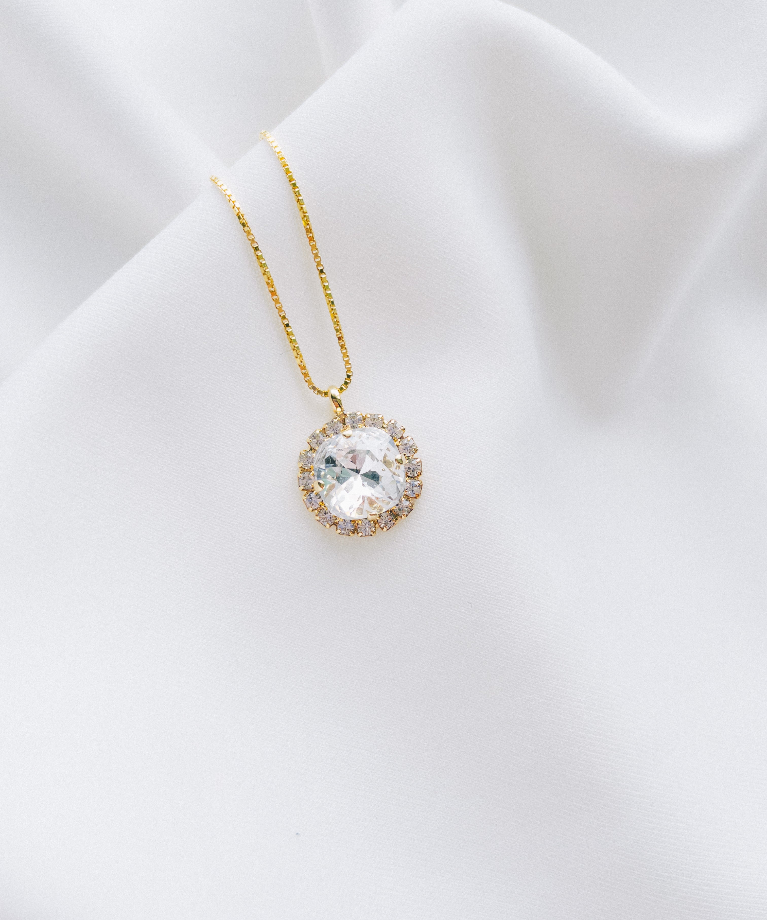 A gold-plated necklace with a round pendant, handset with beautiful crystals, displayed on a white fabric surface.