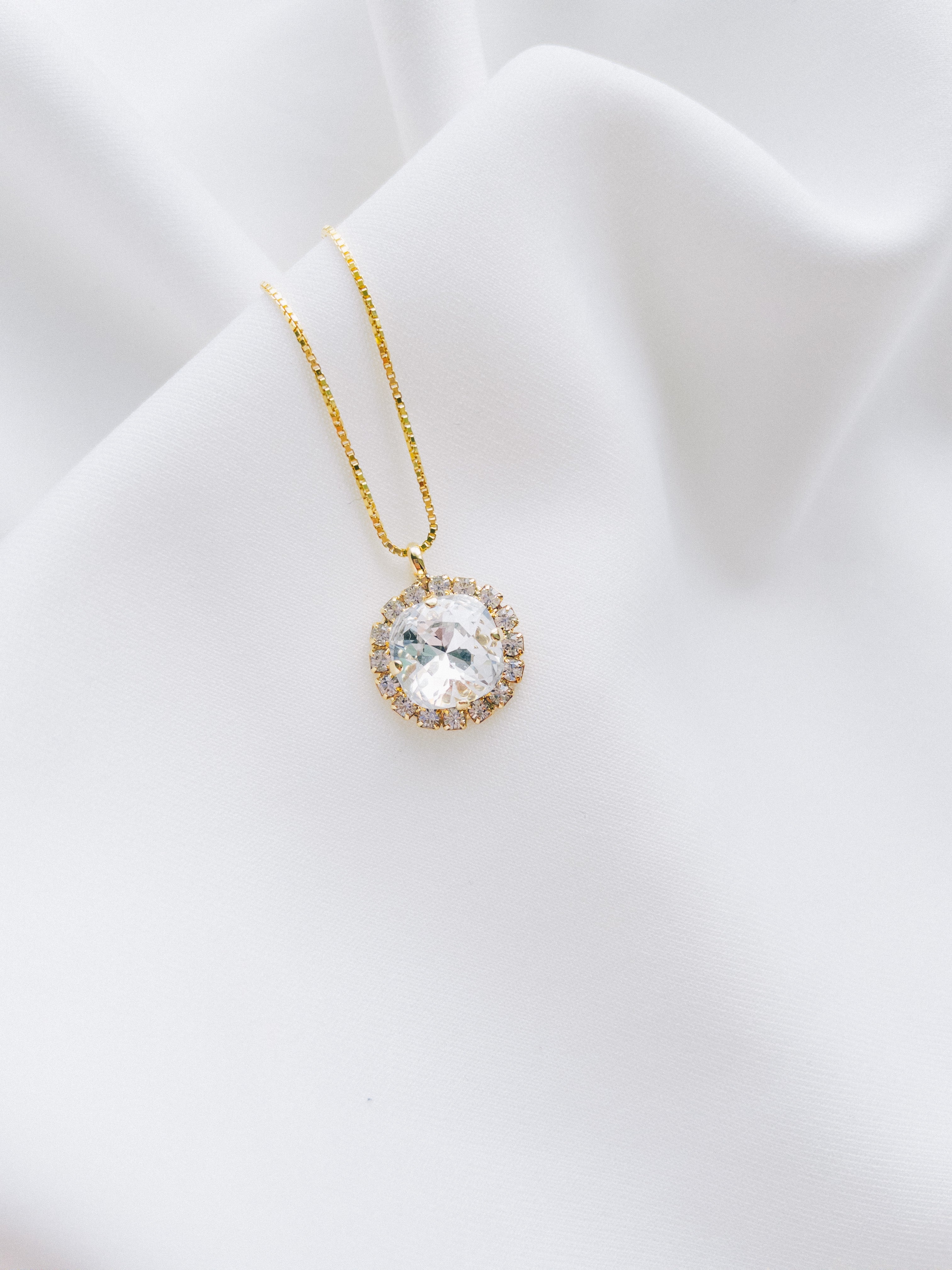 A gold-plated necklace with a round pendant, handset with beautiful crystals, displayed on a white fabric surface.