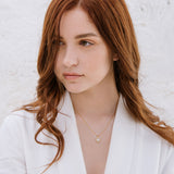 A woman with red hair wearing a white blazer, featuring a duchess necklace with a central oval crystal surrounded by smaller crystals.