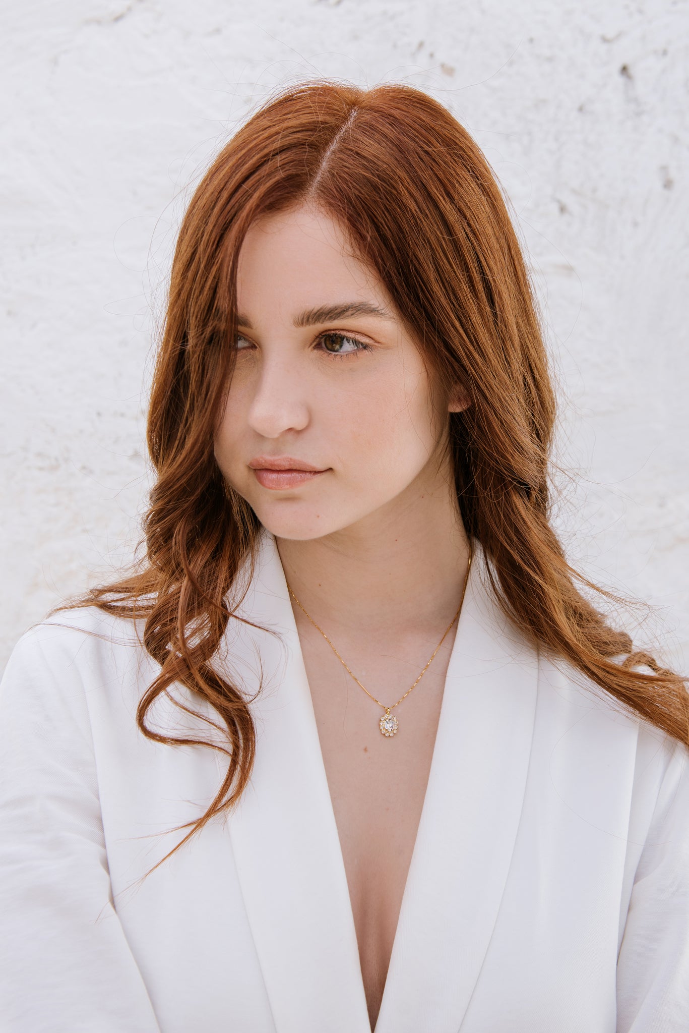 A woman with red hair wearing a white blazer, featuring a duchess necklace with a central oval crystal surrounded by smaller crystals.