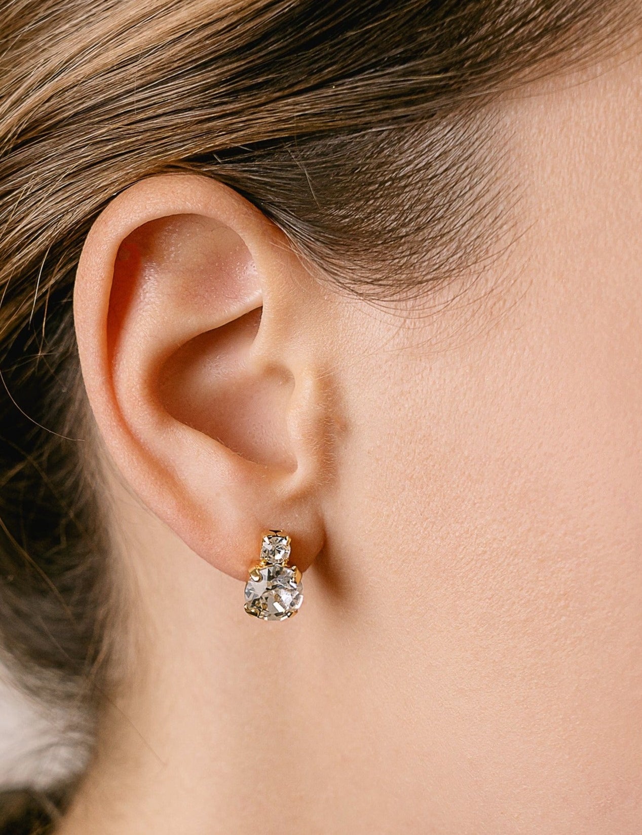 A close-up image of a woman's ear wearing a silver stud earring with a clear crystal.