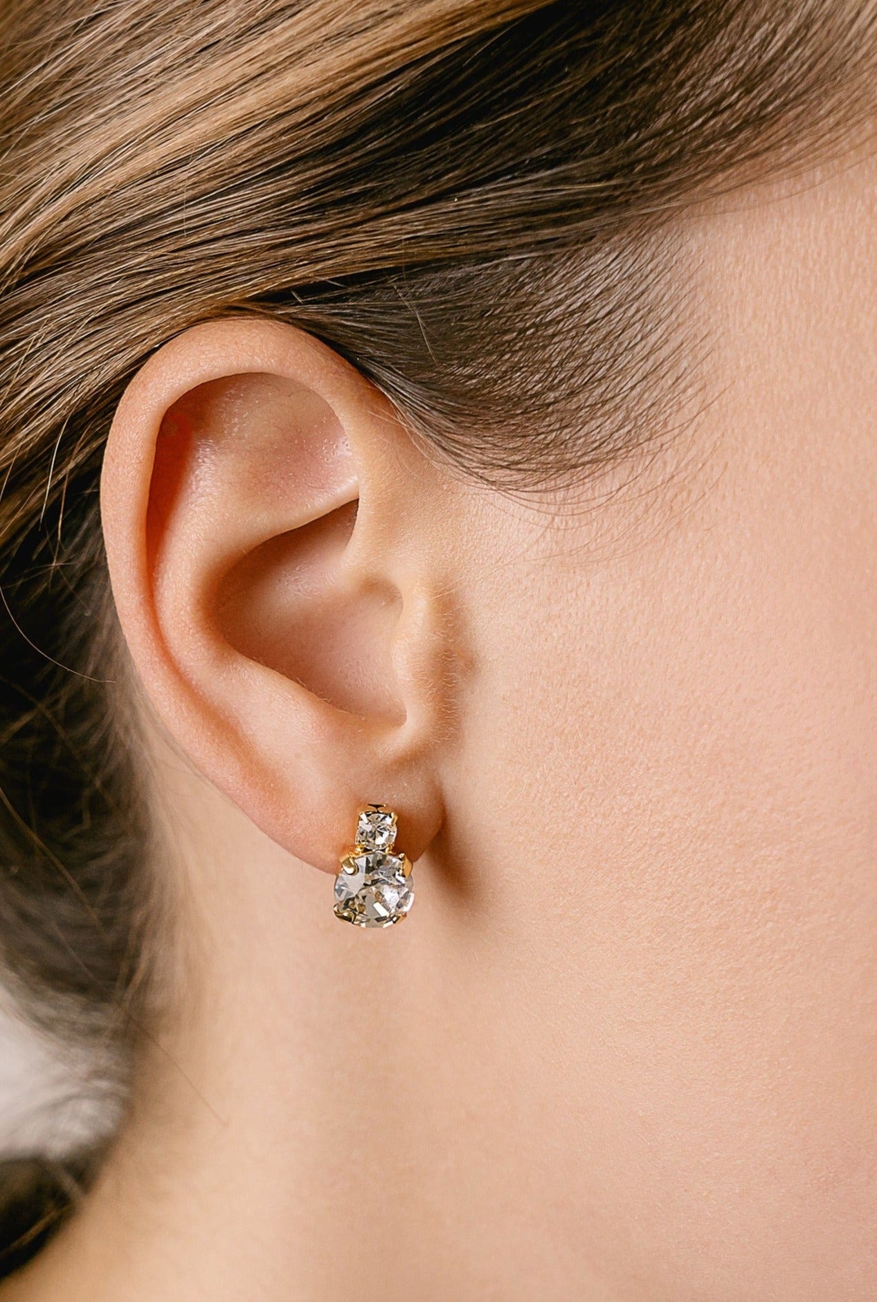 A close-up image of a woman's ear wearing a silver stud earring with a clear crystal.