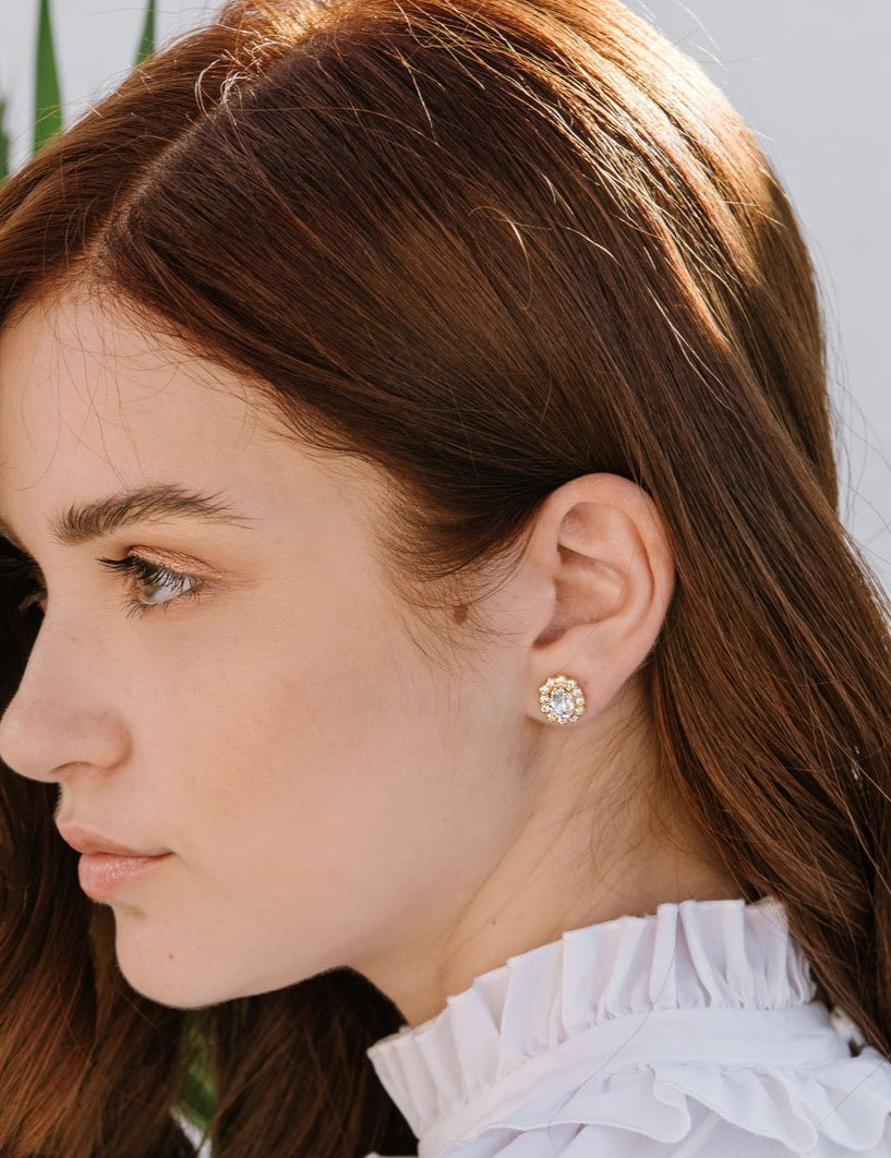 A woman wearing a white top with a crew neckline, showcasing emerald green earrings surrounded by clear crystals.
