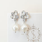 A pair of silver earrings featuring baroque pearls and sparkling crystals, placed on a white card with the logo 'SARAH GAUCI'.