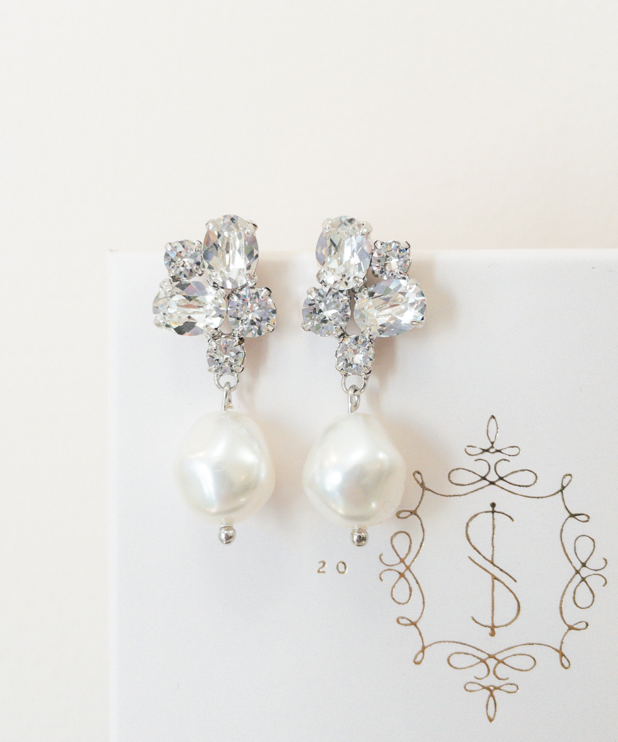 A pair of silver earrings featuring baroque pearls and sparkling crystals, placed on a white card with the logo 'SARAH GAUCI'.
