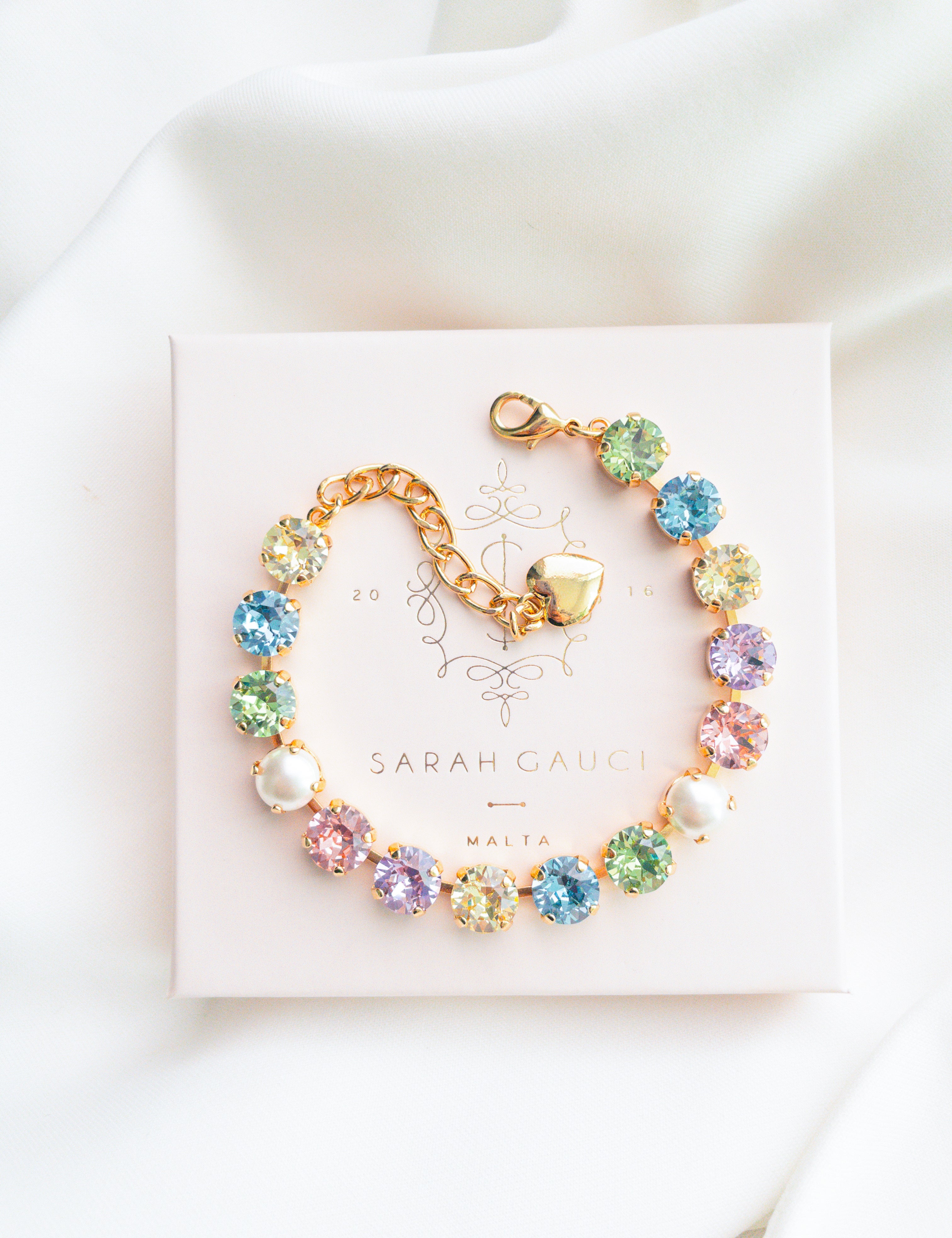 A gold-plated bracelet adorned with multicolored crystals set in a star pattern, presented on a white card with 'SARAH GAUCI' written at the top.