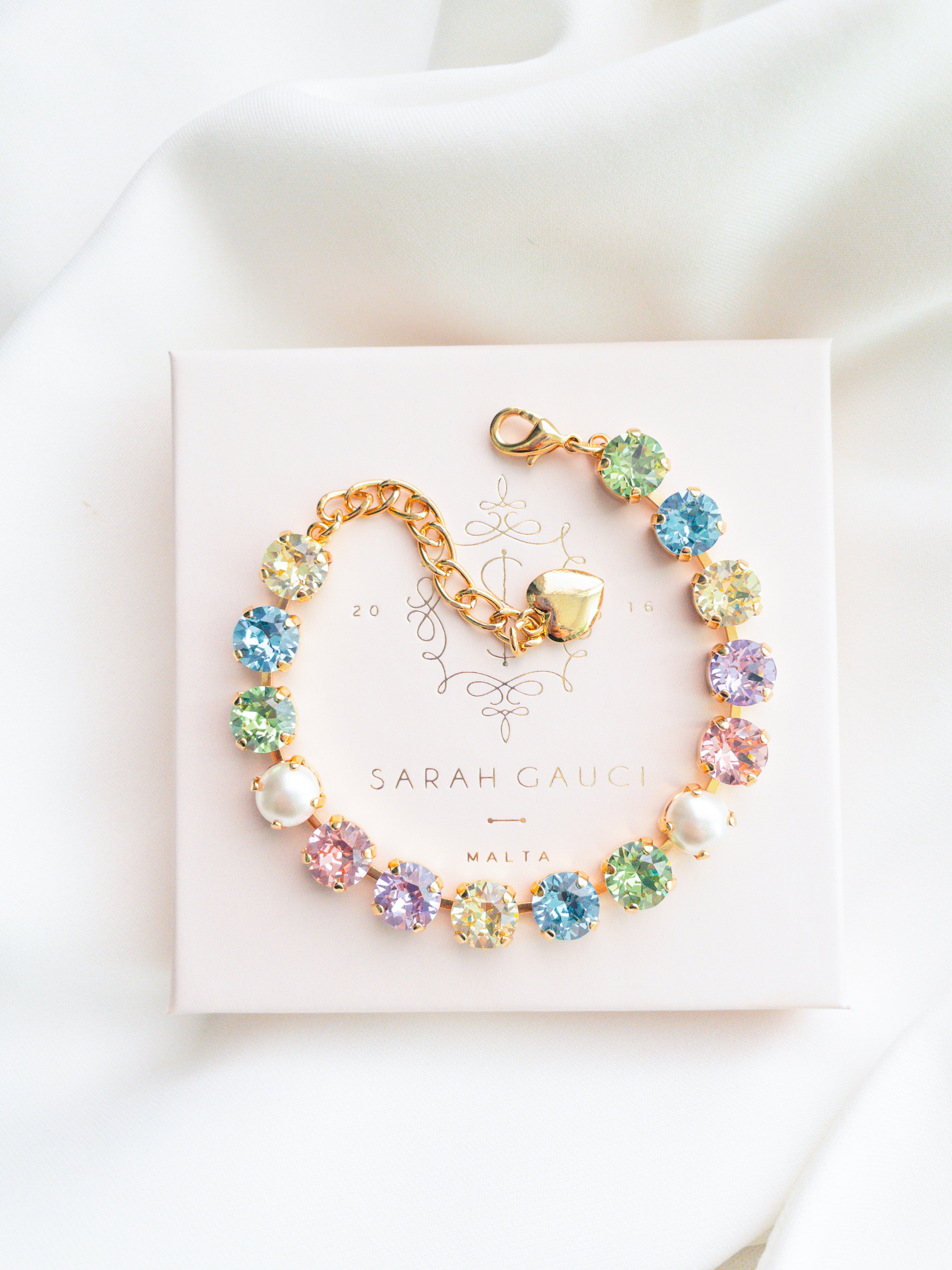 A gold-plated bracelet adorned with multicolored crystals set in a star pattern, presented on a white card with 'SARAH GAUCI' written at the top.